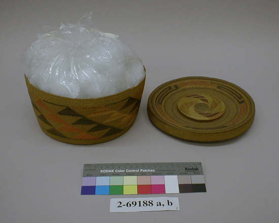 Hearst Museum object titled Basket and lid, accession number 2-69188a,b, described as (a) Basket. Round with stepped triangle design in dark brown and faded orange. (b) Lid has circular geometric design in same colors, handle of lid woven so as to form an enclosure with rattle; underside shows bands of dark blue and purple now faded away on outside. Warp and weft of spruce root, woven and plain twined, false embroidery with white grass, dyed.