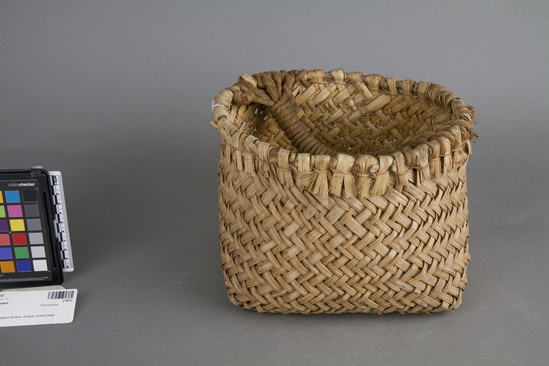 Hearst Museum object 3 of 3 titled Basket, accession number 2-8932, described as Made of yucca. Natural color; square bottom and round rim. Twilled split yucca fibers in body; rim is laid on rod with body splits folded over it and twined in place with bast. Handle made of twine/rope strands affixed to side(s) of basket, then used as foundation for half-hitch coil covering.