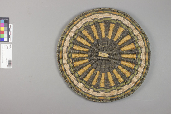 Hearst Museum object 3 of 3 titled Plaque, accession number 2-48552, described as Wickerweave; radiating black and yellow lines from black center; alternating green and yellow areas inside perimeter. Made of ribs of sumac or willow twigs, rabbit brush weft, yucca leaf wrapped edge.