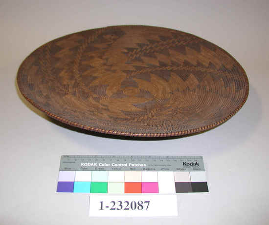 Hearst Museum object titled Winnowing tray, accession number 1-232087, described as Coiled, shallow circular tray.  3-rod foundation. Peeled shoot foundation rods. Complex diagonal patterns in redbud material spiral out from center, alternate dark and light stitches on rim. Split peeled shoots and split redbud shoots.