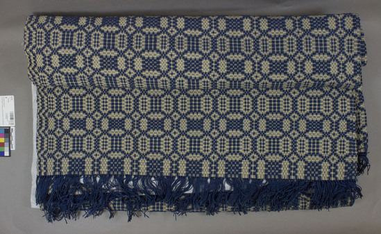 Hearst Museum object titled Coverlet, accession number 2-62165, described as Coverlet? Materials:  linen, silk. Techniques: Plain weave, brocaded, fringed with ends of brocading yarns. Blue and white colors. 60 x 94”. American Colonial design “Sun, Moon, Stars”.