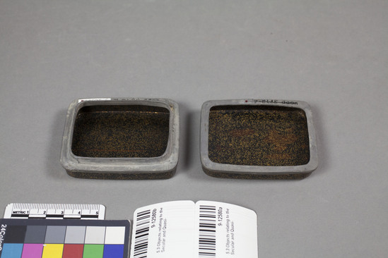 Hearst Museum object titled Box, accession number 9-12580a,b, described as Incense box, lacquer: small, rectangular, lid has slightly rounded top.  Flat bottom. Lid and bottom are equal halves, and each has pewter rims.  Decoration on top of lid depicts a lute (biwa), 2 cymbals, and a reed organ (sho) on a ground of lightly sprinkled gold on black (maki-hanashi) which covers rest of box, inside and out.  Lute: densely sprinkled gold (fundame) imitating wood grain.  Strings and detail in slight relief gold (hiramakie), keys of inlaid mother of pearl.  End has small squares of gold, inlaid (okibara-me). Cymbals: fundame.  Organ of brown lacquer. Tassels in red (e-urushi).  Height 2.5 cm; Length 7.3 cm; Width 5.7 cm.