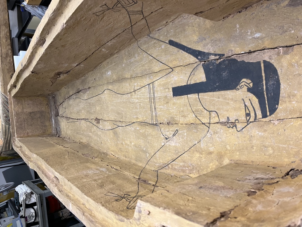 Hearst Museum object 7 of 167 titled Coffin, accession number 6-19912, described as Wooden anthropoid coffin. Inscription running down center of lid. Determined by Kea Johnston to probably be the outer coffin of Iwefaa (6-19928, 12-11039). According to Kea Johnston, "This coffin belonged to a man named Iwefaa, whose name is inserted in the middle of the spells written in the two columns on the front. This coffin is likely the outer coffin for PAHMA 6-19928 based on the similarity of the owner's name, unusual costume, and the paleography of the inscription. Both coffins were purchased on the antiquities market by George Reisner for Phoebe A Hearst. However, stylistically, they are very similar to a set of coffins known to have come from the site of Akhmim, which was excavated in the 1880s by Gaston Maspero, and which has heavily looted for the antiquities market during this decade." "The pectoral vignette between the text and the collar shows the deceased standing before squatting baboon and is the source of our logo. The hieroglyph for 'sky' is above their heads, and the side borders are formed by a pyramid and the symbol for the West.