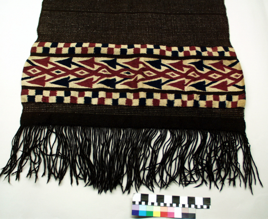 Hearst Museum object titled Chamarro, accession number 3-122, described as Indian zarape or chamarro; 3-122 the same as 3-121 above except that a natural brown instead of black wool was used; it appears older and more worn, also less heavy; approximately 1 m 68 cm long plus 20 cm fringe, 81 cm wide [3-121 tapestry and twill weaves; natural black and white wool with red and blue dyed design in red, white, and blue; also black and white twill pattern; warp form fringes on ends]