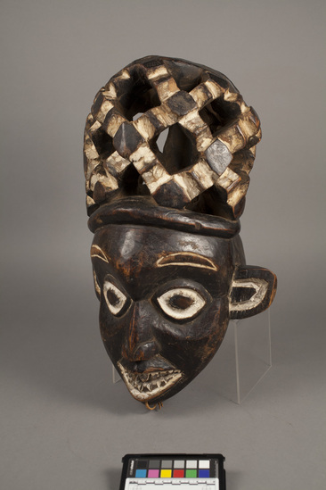 Hearst Museum object titled Helmet mask, accession number 5-5997, described as anthropomorphic mahogany helmet mask with carved features accentuated by white kaolin; carved wood openwork "hair" in spider motif; H. 50 cm.