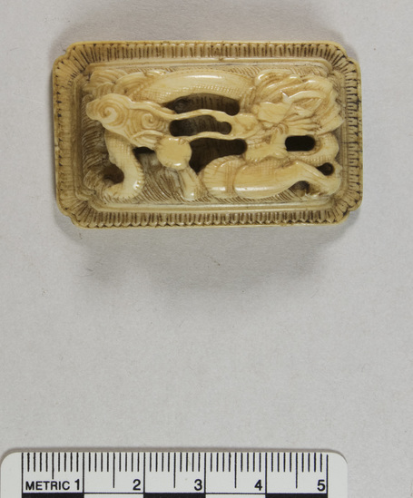 Hearst Museum object 8 of 8 titled Belt clasp, accession number 9-21334, described as Ivory belt clasp. Dragon straining for the pearl of perfection; in high relief on raised platform over 5 x 3 cm platform with notched corners and a border of long loops. Notch for closing dovetail in back.