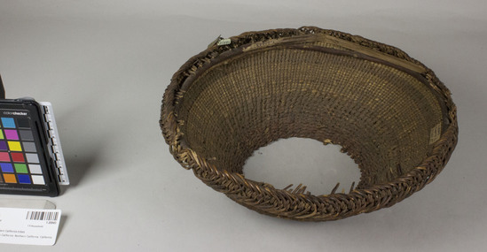 Hearst Museum object 2 of 3 titled Hopper, accession number 1-20843, described as Twined basket hopper.  Paper tag "Klamath R. Tribes Att."  Brass tag "13".  Second paper tag "NW Calif". Per Ralph Shanks:  Twined basket mortar hopper, probably used.  The warp material is reddish, with some remaining bark, but unknown. The background weft is conifer root (Pinophyta) as well as a few wefts of unknown material at the base.  The weft overlay is beargrass.  At the base there is 1 inch of plain twining, over 1-2 rods, followed by 4 weft rows of three strand twining, followed by two weft rows of lattice twining, followed by 1.5 inches of plain twining.  After that there are two weft rows of lattice twining, followed by plain twining to the rim.  The rim consists of braided warps, bound down on the interior; the warps are trimmed nearly flush with the rim.  The rim has a reinforcing rod on the interior.  The design is comprised of two solid bands of beargrass (Xerophyllum tenax). The basket has an exterior workface with a rightward work direction. The basket has an up to the right slant of weft twist.  The overlay is primarily on the outside.  The basket is from Northwestern California.