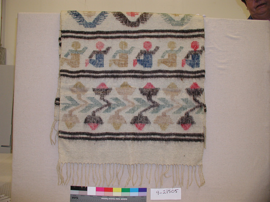 Hearst Museum object titled Shawl, accession number 9-21505, described as Shawl; with 4 cm knotted fringe;  heavy wool, ecru background with 5 figured bands composed of flowers (2) with leaves, people (children) (2), and geometric (diamond) shapes (1), in red, blue, green, dark-brown, and light-brown separated by double bands of 2 dark brown stripes; discontinuous supplemental weft designs; definite back and front face to design;