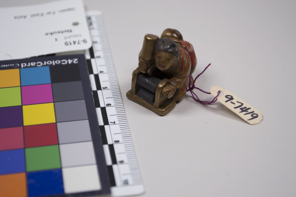 Hearst Museum object titled Netsuke, accession number 9-7419, described as Netsuke: woman at work at her washing. Boy in red behind her.