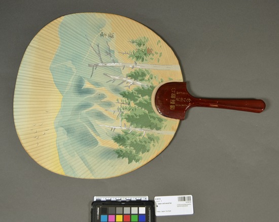 Hearst Museum object titled Fan, accession number 9-16174, described as Paper fan with lacquered wooden handle; round; cream colored background with painted design of buildings, and trees with mountain in background; primary colors; green, blue and gold; calligraphy in upper left corner; on opposite side, silver design in center of fan with “Imperial Hotel Tokyo Japan”; also metal ring at top of base of handle.