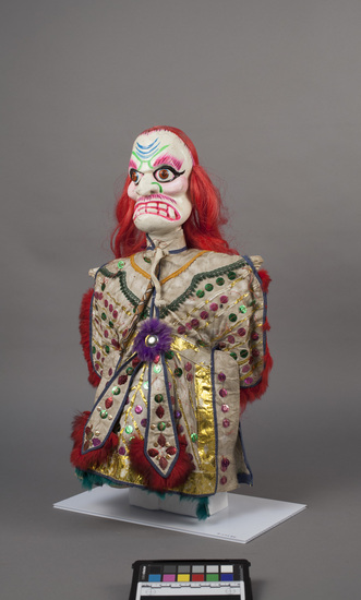 Hearst Museum object titled Hand puppet, accession number 9-22286, described as Puppet, hand.  Ghost.  A.  Head:  carved wood,   white with pink, green and black features, red hair.  B. Body:  cloth, white.  Legs:  cloth, red.  Hands:  wood, white.  Boots:  wood, black.  C.  Robe:  cloth, white with metallic gold trim, green and purple sequins, blue and red rabbit fur trim.  52 x 30 cm (20 1/2 x 11 13/16 in).
