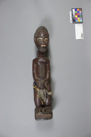 Hearst Museum object 1 of 2 titled Figure, accession number 5-3197, described as Carved wooden figure. Standing male with beard; hands clasped around protruding umbilicum, wearing loin cloth with beaded belt.