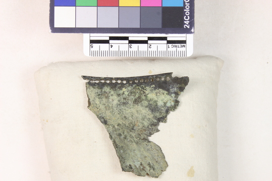 Hearst Museum object 13 of 45 titled Greaves, accession number 8-109, described as Bronze greave and 9 fragments small holes all around edge; serpent and scroll design raised and repousee; greave 41.9 cm long