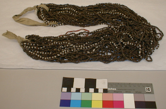 Hearst Museum object titled Necklace, accession number 1-11710, described as Cooked Juniper seeds; multi-strands, five with alternating white glass beads; iris twine, ties together with cotton cloth.