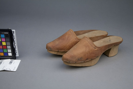 Hearst Museum object titled Slippers, accession number 10-76a,b, described as Slippers with wooden soles and heels and leather tops; no back; connecting strap broken; tooled design on tops; 11 inches long.