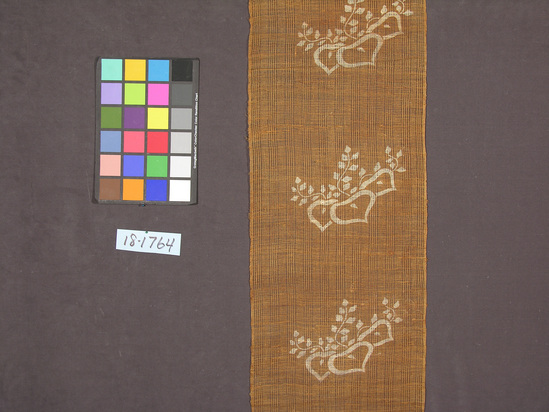 Hearst Museum object titled Textile panel, accession number 18-1764, described as Vegetable fiber panel in spaced plain weave; brown ground with stenciled or printed ecru floral motif, with blossom and vine-like branches; panel is hemmed at one end, with a rod casing at the other.