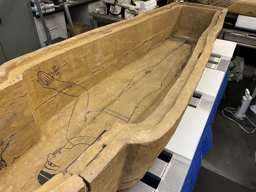 Hearst Museum object 126 of 167 titled Coffin, accession number 6-19912, described as Wooden anthropoid coffin. Inscription running down center of lid. Determined by Kea Johnston to probably be the outer coffin of Iwefaa (6-19928, 12-11039). According to Kea Johnston, "This coffin belonged to a man named Iwefaa, whose name is inserted in the middle of the spells written in the two columns on the front. This coffin is likely the outer coffin for PAHMA 6-19928 based on the similarity of the owner's name, unusual costume, and the paleography of the inscription. Both coffins were purchased on the antiquities market by George Reisner for Phoebe A Hearst. However, stylistically, they are very similar to a set of coffins known to have come from the site of Akhmim, which was excavated in the 1880s by Gaston Maspero, and which has heavily looted for the antiquities market during this decade." "The pectoral vignette between the text and the collar shows the deceased standing before squatting baboon and is the source of our logo. The hieroglyph for 'sky' is above their heads, and the side borders are formed by a pyramid and the symbol for the West.