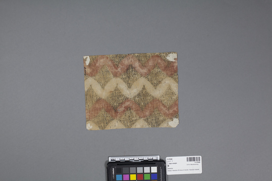 Hearst Museum object 3 of 3 titled Kapa (bark cloth), accession number 11-37049, described as Tapa cloth sample, with design of wavy white and red bands with black diamond filler.  Red bands painted with red vegetable dye; black designs achieved by stamping with charcoal dye.  This "kapa" made from thin "wauke" (Brigham "waoke" p.210) or paper mulberry, Broussonetia papyrifera (pp.119-121).  Reddish color from "noni" (morinda citrifolia) root. (fide Barbara (Kenani) Burns, 3 Aug. 1983).