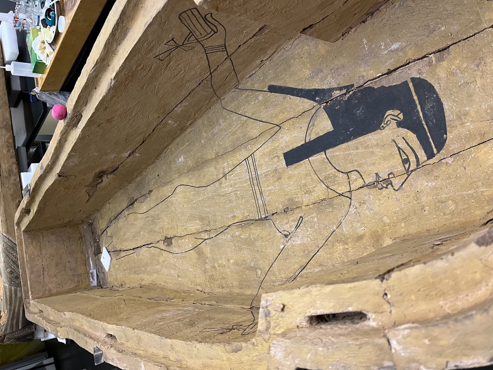 Hearst Museum object 100 of 167 titled Coffin, accession number 6-19912, described as Wooden anthropoid coffin. Inscription running down center of lid. Determined by Kea Johnston to probably be the outer coffin of Iwefaa (6-19928, 12-11039). According to Kea Johnston, "This coffin belonged to a man named Iwefaa, whose name is inserted in the middle of the spells written in the two columns on the front. This coffin is likely the outer coffin for PAHMA 6-19928 based on the similarity of the owner's name, unusual costume, and the paleography of the inscription. Both coffins were purchased on the antiquities market by George Reisner for Phoebe A Hearst. However, stylistically, they are very similar to a set of coffins known to have come from the site of Akhmim, which was excavated in the 1880s by Gaston Maspero, and which has heavily looted for the antiquities market during this decade." "The pectoral vignette between the text and the collar shows the deceased standing before squatting baboon and is the source of our logo. The hieroglyph for 'sky' is above their heads, and the side borders are formed by a pyramid and the symbol for the West.