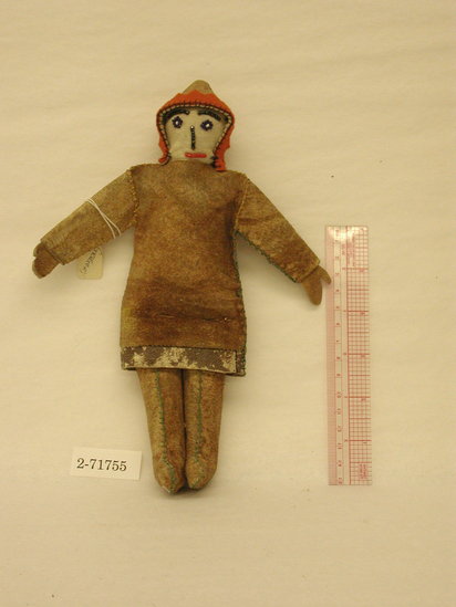 Hearst Museum object titled Doll, accession number 2-71755, described as Dakota-Santee doll.  Fabric stuffed doll, dressed in leather tunic.  Hood had orange-red felt outline. Face made of felt with beaded features.  Flat leather hands.  Sewn w/ embroidery floss in green and yellow.  The tunic at lower edge has a separate piece of leather which might have been furred at one time.  Eyes are of blue beads w/ white in center; black beads for eyes and nose and eyebrows, and red for mouth.  H = 9.5”