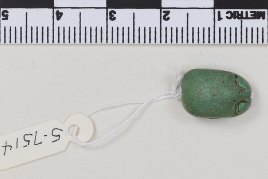 Hearst Museum object titled Scarab seal, accession number 5-7514, described as Seal: Scarab; green faience; no protothorax; rough work; Reverse- hook scroll incised down center with hieroglyph each side; Height 6.4 mm. Length 1.3 cm. Width .9 cm. Note: w3dyt, nb, and red crown are on both sides of the hook scroll.