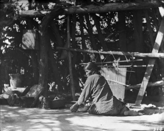 Hearst Museum object titled Black-and-white negative, accession number 15-315, described as closer view of Navajo woman at the loom; note cooking utensils on ground at left