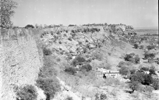 Hearst Museum object titled Black-and-white negative, accession number 15-30513, described as 8 x 10" Black and white negative of the old Gwalior Fort.  Hoefler's original description: "Gwalior State, Central India. The old Gwalior Fort is one of the sights of India. Its founding is veiled in obscurity, the first historical mention being an inscription on a temple of the Sun dated about 525 A. D. Battles and wars have been decided here for centuries and yet it stands rugged and majestic on top of its table mountain with the modern city of Gwalior at its feet. Photo shows the old Palace within the fort wall. The large white building in the foreground at the base of the mountain is the ancestral home of Capt. Sardar Mohammed Shah Hazratji, the Mohammedan A.D.C. to His Highness, who was assigned to the Hoefler party as interpreter and guide."  Verso: Prints Supplied to: International News.