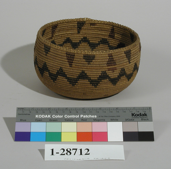 Hearst Museum object titled Bowl basket, accession number 1-28712, described as Coiled, black and brown design, cross-stitch edge. Per Ralph Shanks:  Basket bowl, coiled.  Foundation is three-rod willow.  The background material is willow.  The design materials are redbud and bulrush root.  The designs include a horizontal zigzag band around the center of the basket, triangles at the rim, and rectangles on the base.  The basket has an exterior workface and is woven in a leftward work direction with interlocking stitches.  The weft fag ends are clipped.  The rim is braided with criss-crossed stitch and a slightly tapered coil ending.  The leftward work direction, the interlocking stitch, and the design pattern make this likeley to be a Washoe basket.