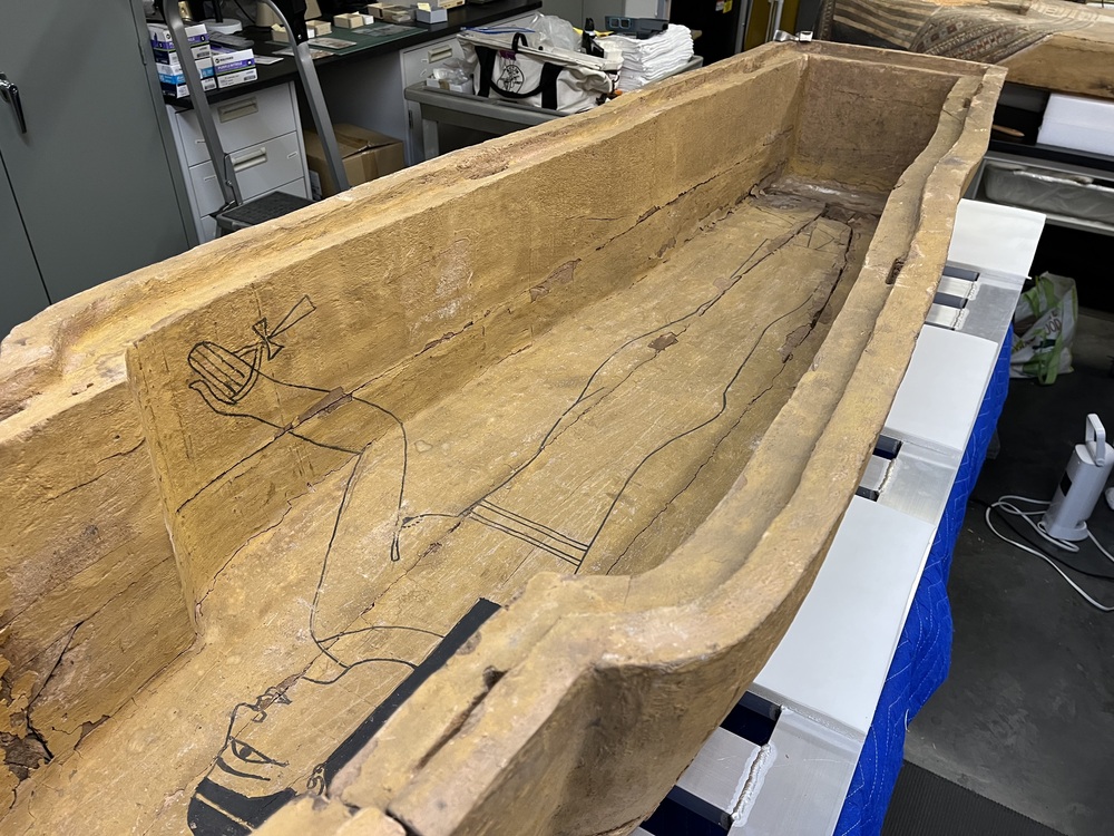 Hearst Museum object 80 of 167 titled Coffin, accession number 6-19912, described as Wooden anthropoid coffin. Inscription running down center of lid. Determined by Kea Johnston to probably be the outer coffin of Iwefaa (6-19928, 12-11039). According to Kea Johnston, "This coffin belonged to a man named Iwefaa, whose name is inserted in the middle of the spells written in the two columns on the front. This coffin is likely the outer coffin for PAHMA 6-19928 based on the similarity of the owner's name, unusual costume, and the paleography of the inscription. Both coffins were purchased on the antiquities market by George Reisner for Phoebe A Hearst. However, stylistically, they are very similar to a set of coffins known to have come from the site of Akhmim, which was excavated in the 1880s by Gaston Maspero, and which has heavily looted for the antiquities market during this decade." "The pectoral vignette between the text and the collar shows the deceased standing before squatting baboon and is the source of our logo. The hieroglyph for 'sky' is above their heads, and the side borders are formed by a pyramid and the symbol for the West.