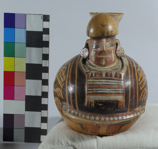 Hearst Museum object titled Bottle, accession number 16-12114, described as Pottery bottle with flaring spout; effigy of a man with bag slung around neck; red and white slip and resist painted designs. Has been waxed