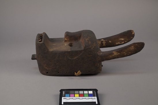 Hearst Museum object titled Mask, accession number 5-16127, described as Ibo Mask; carved, painted wood, assymetrical with two straight horns; colors, red, white and black; perforated along edges for rafia or drape attachment. Conservation: 2 small pegs behind horns broken, paint chipping, 6 upper teeth missing, crack in lower edge ending in a hole, hole at crown. Ibo Mask (Udi, 1, 400, 1945) Simple, old, Red-White-Black, assymetrical, straight horns.