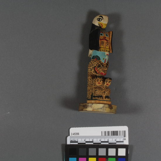 Hearst Museum object 1 of 3 titled Totem pole model, accession number 2-45356, described as Carved and painted wood totem pole model; top half is bird with recurved beak, black and white exterior pigmentation, also red, yellow, and light blue pigment used; fish below; bottom half is a seated bear. Written in back in ink is: "Eli T (? ) Metlakatla Alaska".