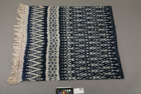 Hearst Museum object titled Shawl, accession number 16-20337, described as Indigo and ecrie ikat woven ecru; knotted warp fringe, hand loomed. 2 zig-zag designed bands at each end. Overall pattern in center. Finely woven. Cotton woven, indigo dye.