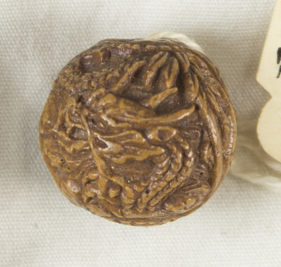 Hearst Museum object titled Netsuke, accession number 9-12451, described as Japan. Ojime, brown bead, with ornate decoration of tiger (tora) and dragon (tatsu) in a bamboo forest. Apparent seam between halves. Diameter 1.7 centimeters.