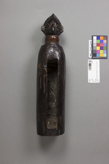 Hearst Museum object titled Gong, accession number 5-15397, described as Slit gong, wood, hand carved from solid tree limb, round, well-patinated; finial/stylized carved human head at top; lower two thirds hollowed out. Length 36.9 cm. Diameter (at base) 8.5 cm. Used by a diviner to announce his entry into a village.