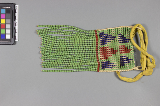 Hearst Museum object titled Pubic apron, accession number 5-6911, described as Native name: Kitemu-apron w/belt Pubic apron; green, red and blue spherical glass beads strung on twisted fibre twine in rectangular shape with several strands of green beads only dangling from bottom; belt of yellow cloth; l. 27 cm, w. 13.5 cm. Materials: cloth; buttons, beads, fiber Women by women as clothing suspended over genital region and tied around waist. Kitemu is an apron with a belt. An apron without a belt is called Kisanza. A diminutive child's apron is also called Kisanza. Made by women