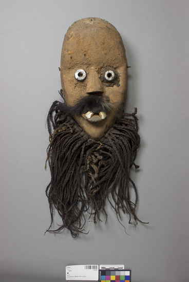 Hearst Museum object titled Mask, accession number 5-3316, described as Carved wooden face mask. Human face with buck teeth and moustache. Eyes outlined with metal. Braided hair fringe attached.L = 11.0”