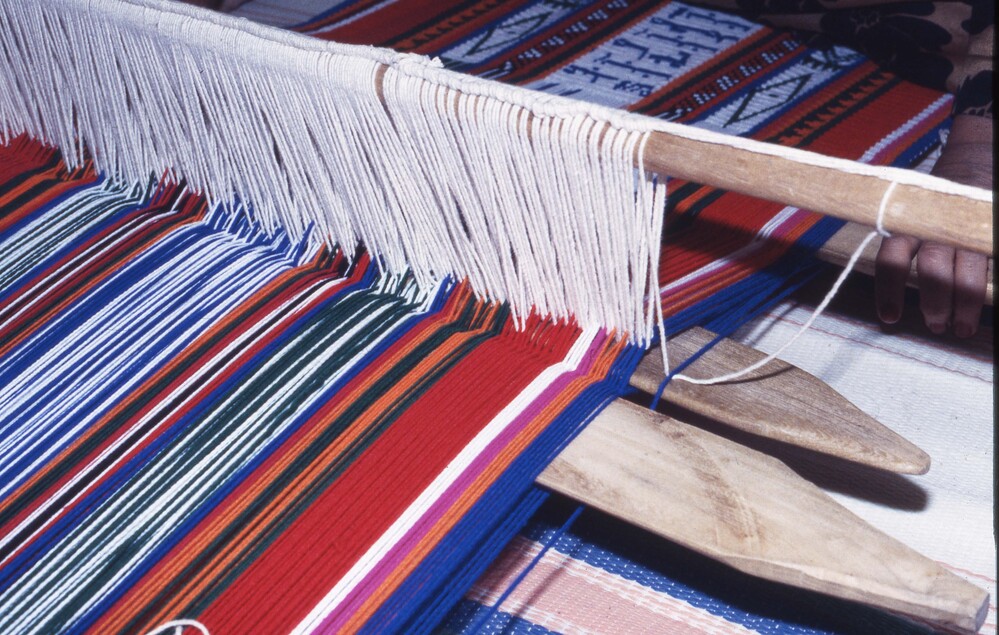 Hearst Museum object titled Color slide, accession number 25-99563, described as 35mm color slide transparency. Close-up of a person's hands weaving on a loom.