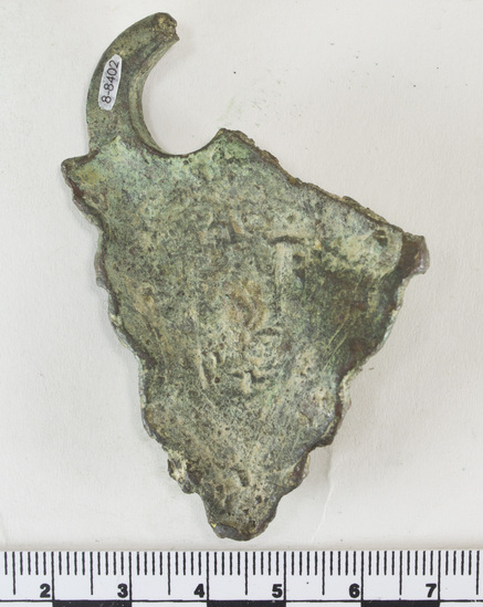 Hearst Museum object 4 of 6 titled Oil lamp fragment, accession number 8-8402, described as Fragment of lamp handle, bronze; face in low relief surrounded by decorative curls of hair and bear; broken loop on upper right; green patina on front and back. Max. L.; 6.8 cm.