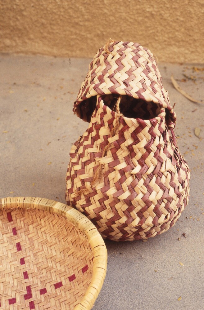 Hearst Museum object titled Color slide, accession number 25-98645, described as 35mm color slide transparency. 2 woven baskets. Basket on the left is shallow with an "x" design and a small handle. Basket on the right is pear-shaped with a lid and a small handle.