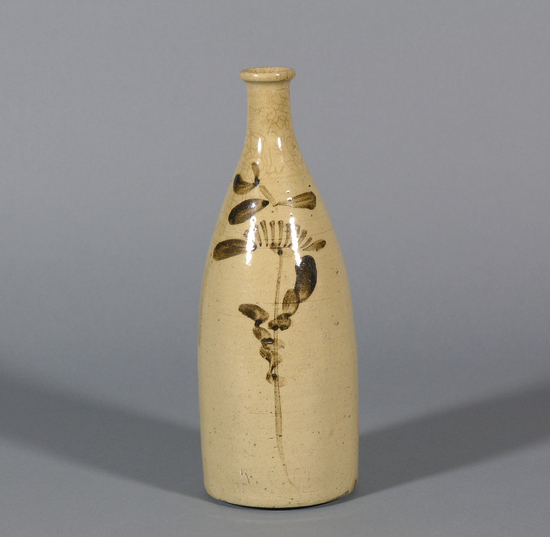 Hearst Museum object titled Sake bottle, accession number 9-12296, described as Sake bottle; creamy color decorated with long-stemmed flower done in free brush strokes. Plain side very pitted. Can see unglazed spots where bottle was held in glazing. Height 10.5 inches, base 3.75 inches.
