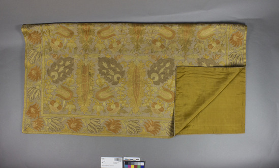 Hearst Museum object titled Bed hanging, accession number 9-15040, described as Bed hanging.  Cotton, silk, silk lining.  Plain weave, embroidered in "atlama stitch", plain weave lining.  Natural ground, green, yellow, and orange designs, orange lining. Floral motives.  46 inches by 33 inches.