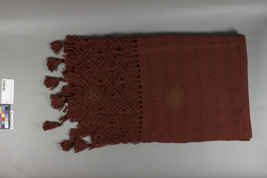 Hearst Museum object titled Shawl, accession number 16-20225, described as Shawl; 156  x 65 centimeters; fringe 21 centimeter excluding tassels; tassels 5 centimeter., reddish brown solid ground with weft spacing; fringe warped thread knotted with 8 tassels on one end and 7 tassels on other end.