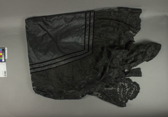 Hearst Museum object titled Shawl, accession number 7-7162, described as Shawl; silk; taffeta, velvet ribbon trim; lace ruffle plus wide lace panel at one side; black; 49 x 82.5 inches at greatest length. Floral motives in lace.