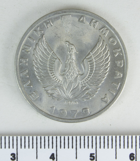 Hearst Museum object titled Coin, accession number 7-6115, described as Coin; bright, silvery metal; 20 drachmai; size: 29 mms; weight: 11.2620 grms,; mint condition Obverse: Helmeted head of Athena, left; in field, right 20 PX; in field, left, N. (name of designer?) Reverse: Phoenix; below I. and date 1973; in field circling phoenix, . Latter wording also appears around edge of coin