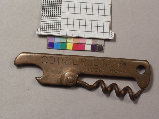 Hearst Museum object titled Bottle opener, accession number 2-68954, described as Key ring advertising giveaway, 20th Century. Corkscrew/caplifter combination; copper plated steel sheet stock folded in half into handle; crown caplifter at one end, hole at opposite end; helical wire worm pivoting on rivet at center; handle die stamped "Copper Club Butte, Mont."; 7.3 cm long