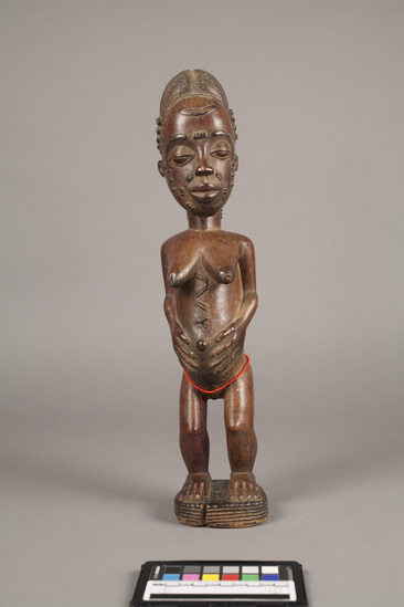 Hearst Museum object 4 of 7 titled Figurine, female, accession number 5-3182, described as carved wooden figure; standing female with hands clasped around protruding umbilicum; string of red beads around thighs;