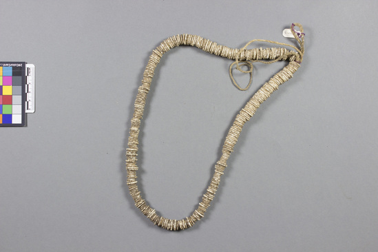 Hearst Museum object titled Necklace, accession number 5-13329, described as Intore., Kenya, Gob Dogo, Rendille. Summer, 1977. 5-13329, acc no. 3332. File code: 2.2 Collector: Jean Colvin. Donor: Jean Colvin. Materials, techniques: Ostrich egg shell- break into small pieces and press a central hole with an awl- string them and rub between 2 stones- children taking care of animals often find egg shells. Context of use: Made by women; won around waist- a beaded apron hangs from it to cover genitals-sometimes worn alone- worn by girls 3-10 years old. Description: Waistband; ostrich egg shell; disk shaped beads on strings; L=64 cm.  References: for additional information see field sheets in acc. env.