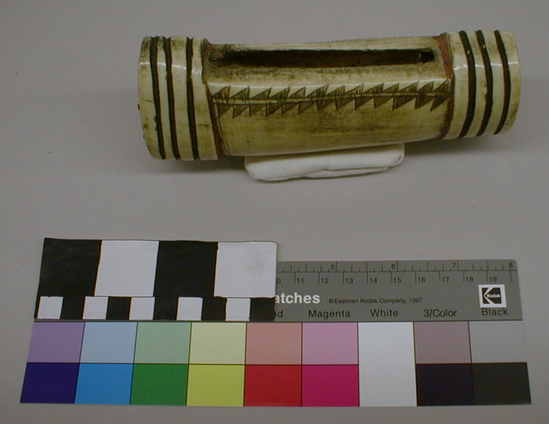 Hearst Museum object titled Money purse, accession number 1-1223a-c, described as (a) Money purse. Elk antler, hollow; raised flange with 3 deep grooves at each end; longitudinal slit at center; double row of triangles at sides. (b) Cover for (a), splint, rectangular, hole at one end, undecorated. (c) Leather thong attached to (b).