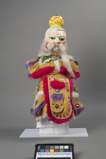 Hearst Museum object 6 of 8 titled Hand puppet, accession number 9-22424, described as Puppet, hand.  Taoist.  A.  Head:  carved wood, light pink, red mouth, green, brown and black features, painted gray hair,  long white hair, beard and moustache, yellow and orange lotus crown.  B. Body and legs:  cloth, white.  Hands:  wood, white, pink nails.  Boots:  wood, gray and white.  C. Robe:  cloth, yellow, green cape, gold, silver, red and blue mirrow, dark pink, white and purple rabbit fur trim.  49 x 24 cm (19 5/16 x 9 7/16 in)